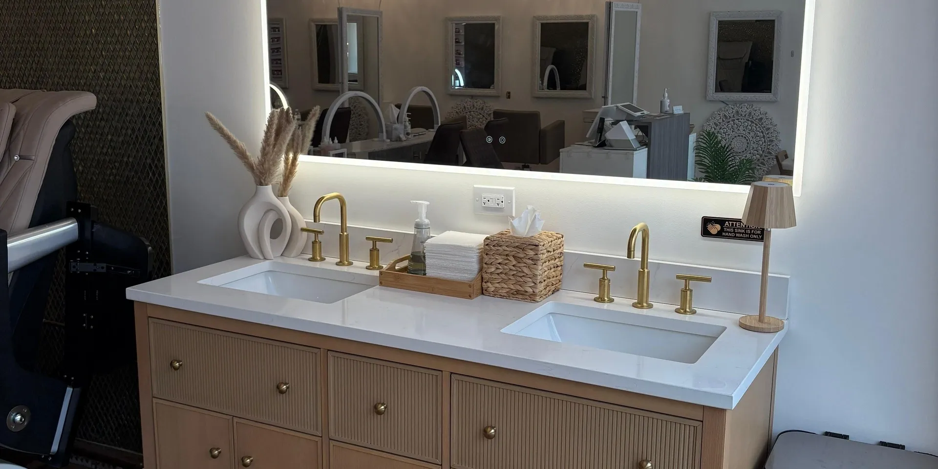 Salon vanity with twin sinks, warm gold fixtures, and a large illuminated mirror